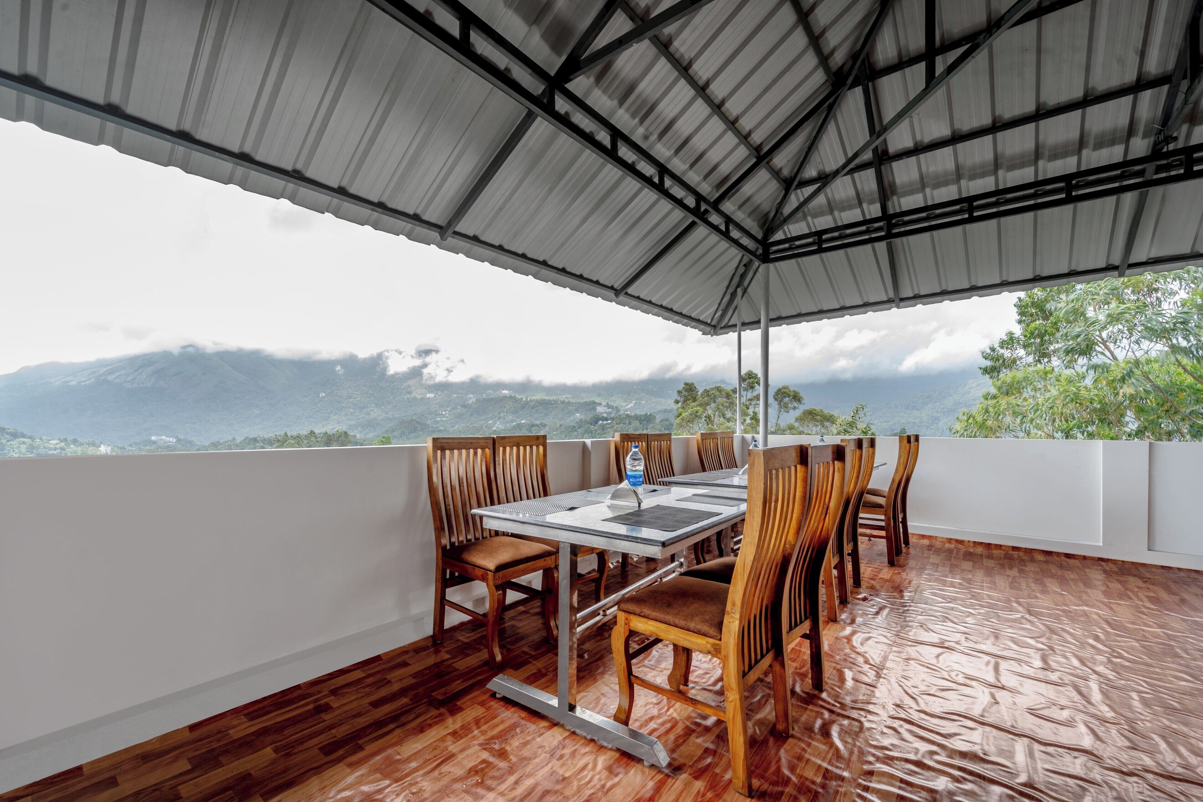 A covered outdoor dining area with a table and chairs, overlooking a mountainous landscape.