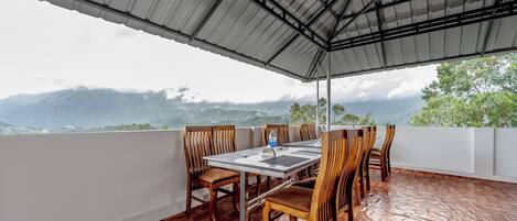 A covered outdoor dining area with a table and chairs, overlooking a mountainous landscape.