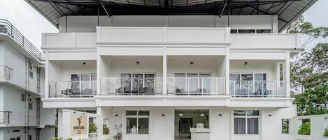 Un edificio de varios pisos con balcones, un acceso cubierto y macetas con plantas.