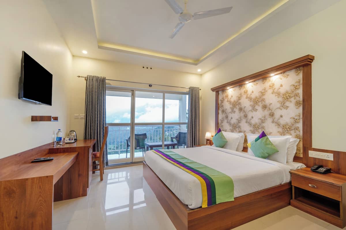 A hotel room with a large bed, a desk, a chair, a TV, and a balcony with a view.