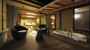 A room with a wooden floor, a bathtub, two chairs, a table, and a sliding door leading to another room. - Oyado Zuiyo (Atami)