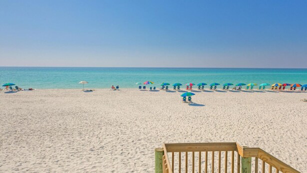 A beach with a wooden boardwalk leading to the water, clear skies, and several colorful umbrellas. - Sandpiper Cove Unit 2063 1 Bedroom Beach Getaway in Destin, FL (Destin)