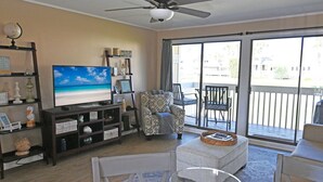 A living room with a television, a sofa, a chair, and a balcony with outdoor furniture. - Sandpiper Cove Unit 2063 1 Bedroom Beach Getaway in Destin, FL (Destin)
