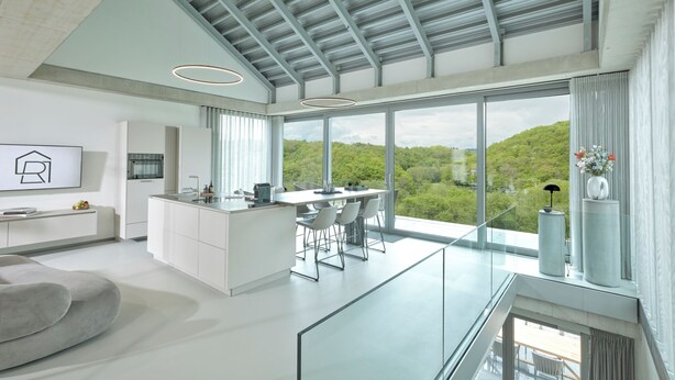 A modern kitchen with a central island, a dining area with chairs, and large windows offering a view of the forest. - Racers Lodge "Grand Prix" with lifting platform and double garage, near Nürburgring  (Bermel)