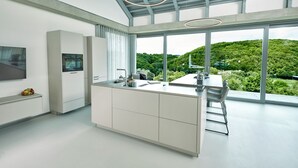 A modern kitchen with a large island, a dining area, and a view of a lush green landscape. - Racers Lodge "Grand Prix" with lifting platform and double garage, near Nürburgring  (Bermel)