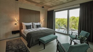 A modern bedroom with a large bed, a bench, and a seating area with chairs and a table. - Racers Lodge "Grand Prix" with lifting platform and double garage, near Nürburgring  (Bermel)