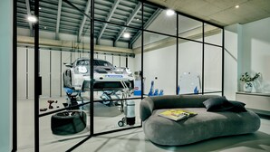 A modern garage with a white sports car on a lift, a grey sofa with a magazine, and a potted plant. - Racers Lodge "Grand Prix" with lifting platform and double garage, near Nürburgring  (Bermel)