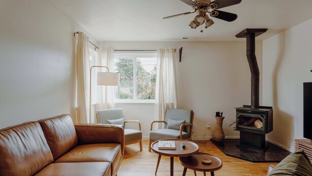 A cozy living room with a brown leather sofa, two armchairs, a coffee table, and a wood-burning stove.