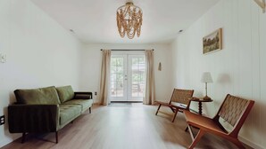 A spacious room with a green sofa, a wooden chair, and a chandelier.