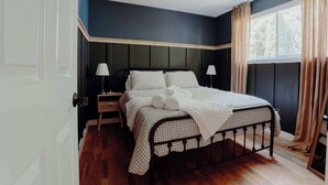A neatly made bed with a checkered bedspread, two bedside lamps, and a window with curtains.