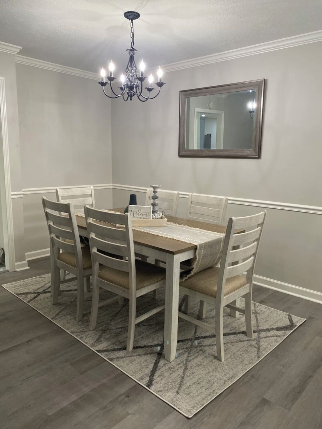 Comedor con mesa y sillas de madera, una araña y un espejo en la pared.