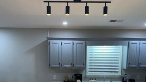 Une cuisine moderne dotée d’un îlot central, de deux tabourets de bar, de meubles de couleur grise, d’une fenêtre avec stores et d’un luminaire au plafond.