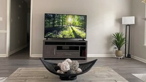 Un salon avec un téléviseur à écran plat posé sur un meuble en bois foncé, un lampadaire moderne et une plante en pot.