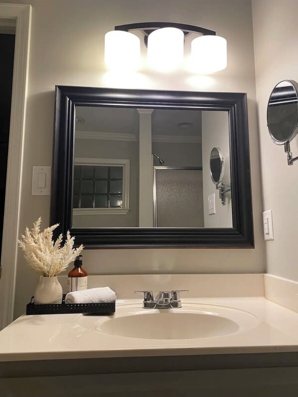 A bathroom with a large mirror, a white sink, a towel, and a decorative vase. - A sweet retreat in the cove… (Jackson)