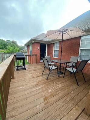 Una terraza de madera con una parrilla, una mesa exterior y sillas.