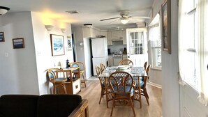 Een eetgedeelte met een tafel en stoelen, een keuken op de achtergrond en een plafondventilator.