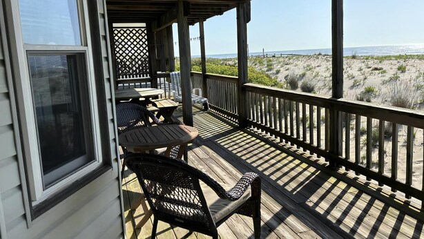 Een overdekt terras met buitenmeubilair en uitzicht op het strand, met een houten balustrade.