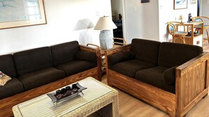 Een woonkamer met twee donkere banken, een rieten salontafel en een houten bijzettafeltje met een lamp.