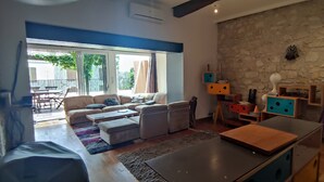 Un saló amb un sofà, una taula de centre, una taula de dinar i una paret de pedra amb prestatgeries.