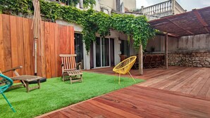 Una terrassa de fusta amb una zona de gespa artificial verda, cadires de fusta i una cadira groga.