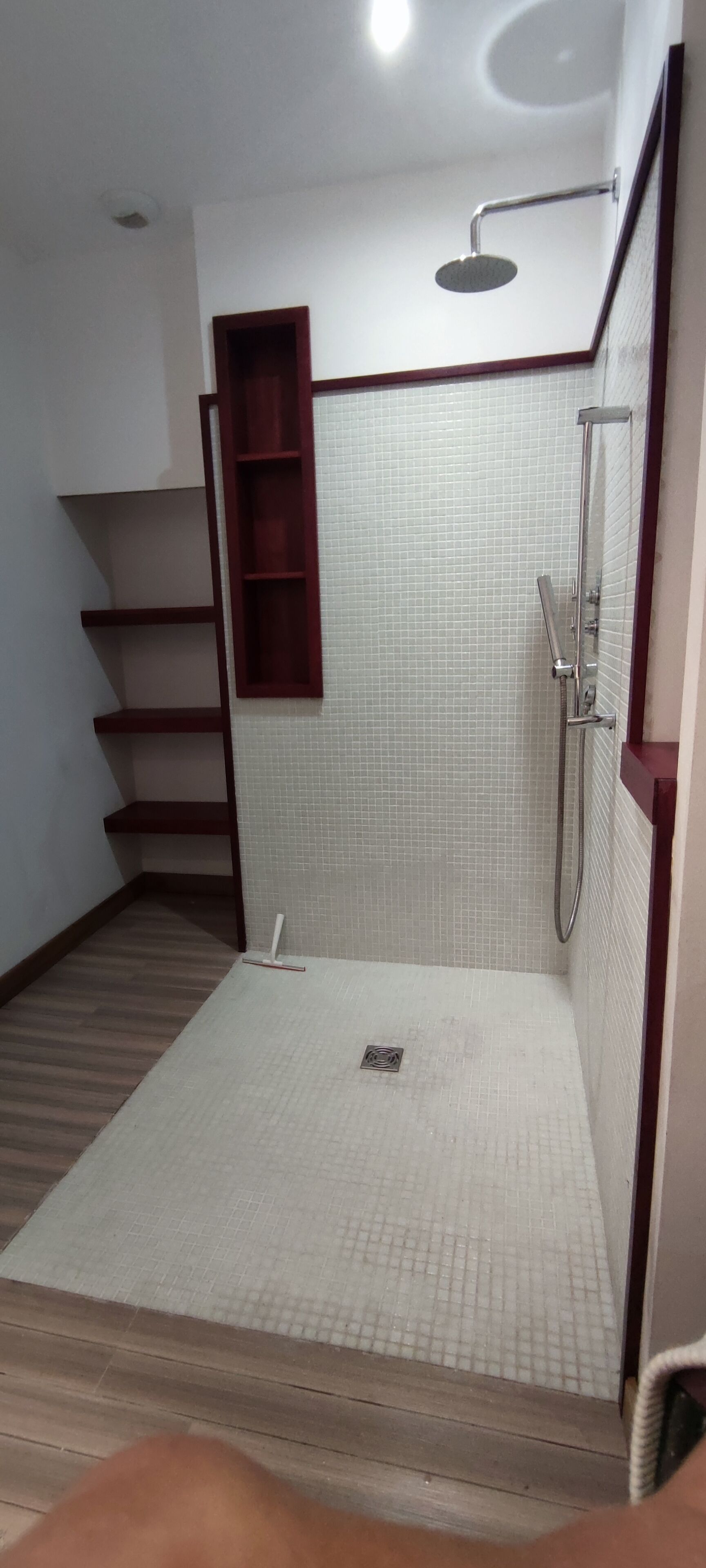 A small, tiled shower area with a wooden shelf and a metal showerhead.
