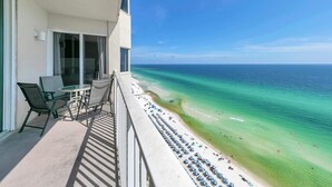 A balcony with a table and chairs, overlooking a beach with clear turquoise water and a pier in the distance. - Tidewater 1802 (Panama City Beach)