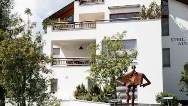 Ein modernes, zweistöckiges Gebäude mit weißer Fassade, Balkonen und einer Skulptur einer Person.