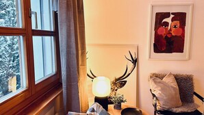Ein gemütliches Zimmer mit einem Holsterfenster, einem Tisch mit Lampe, einem Stuhl und einem gerahmten Kunstwerk an der Wand.