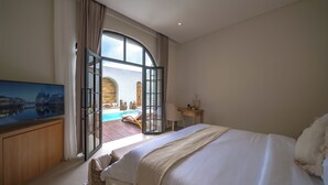 Een hotelkamer met een groot bed, een televisie, een bureau en uitzicht op een buitenzwembad.
