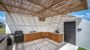 Een moderne buitenkeuken met een ingebouwde barbecue, een spoelbak en een hangende lamp.