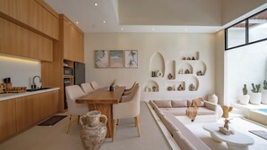 Een moderne keuken met houten kasten, een eethoek met een houten tafel en stoelen, en een zithoek met een bank en een salontafel.