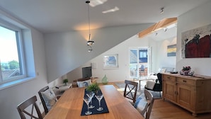 Un vaste espace dédié à la salle à manger, avec une table et des chaises en bois, un lustre, et une vue sur la cuisine et le salon.