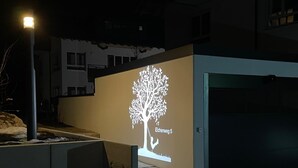 Un bâtiment moderne dont la façade est ornée d’une projection représentant un arbre, et un escalier menant à l’entrée.