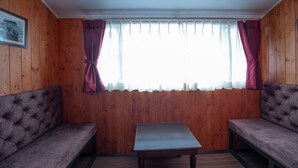 Ein Zimmer mit Holzwandverkleidung, einer gepolsterten Bank, einem kleinen Tisch und einem Fenster mit Vorhängen.