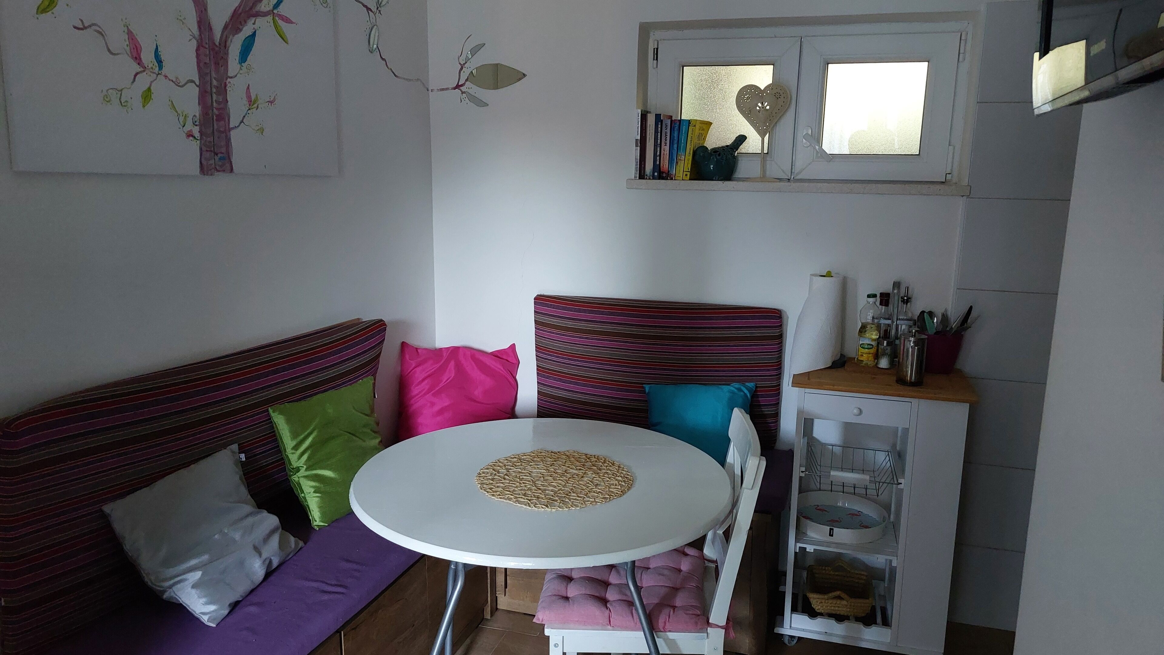 Ein kleiner, gemütlicher Raum mit einem weißen runden Tisch, einem gestreiften Sofa und einem Schrank mit Küchenutensilien.