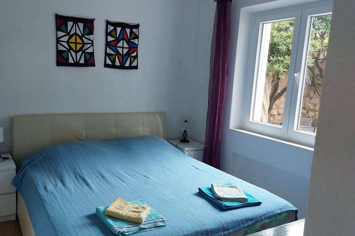 A bedroom with a bed, two wall art pieces, a window with curtains, and a bedside table with a lamp.