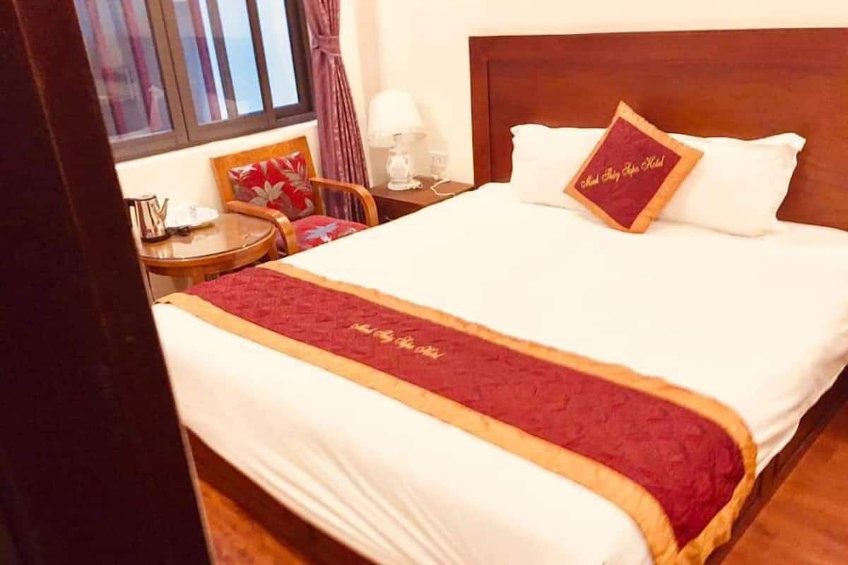 A neatly made bed with a red and gold bedspread, a wooden headboard, and a single decorative pillow with text.