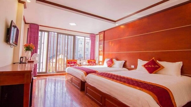 A hotel room with two beds, a desk, a television, and a large window with curtains.