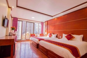 Habitación de hotel con dos camas, un escritorio, un televisor y un ventanal con cortinas.