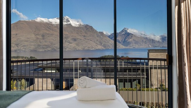 Une chambre d’hôtel dotée d’une grande fenêtre donnant sur un paysage de montagnes et un plan d’eau.