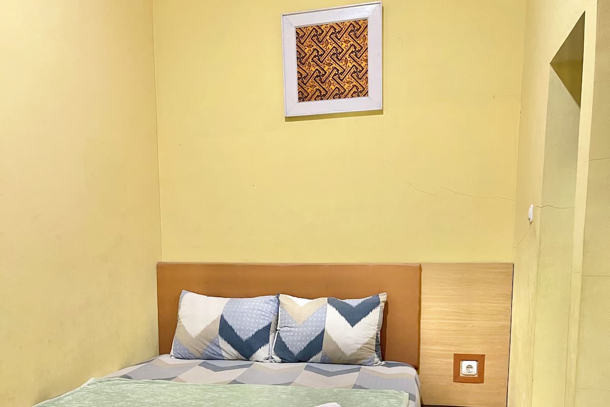 Una cama bien hecha con una colcha estampada y almohadas, una mesita de noche con una lámpara y un cuadro en la pared.