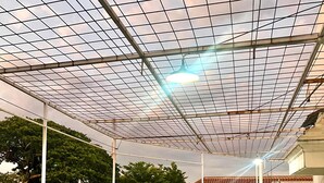 A covered outdoor area with a grid-like ceiling structure, surrounded by greenery and a concrete floor. - Telu Telu Solo (Surakarta)