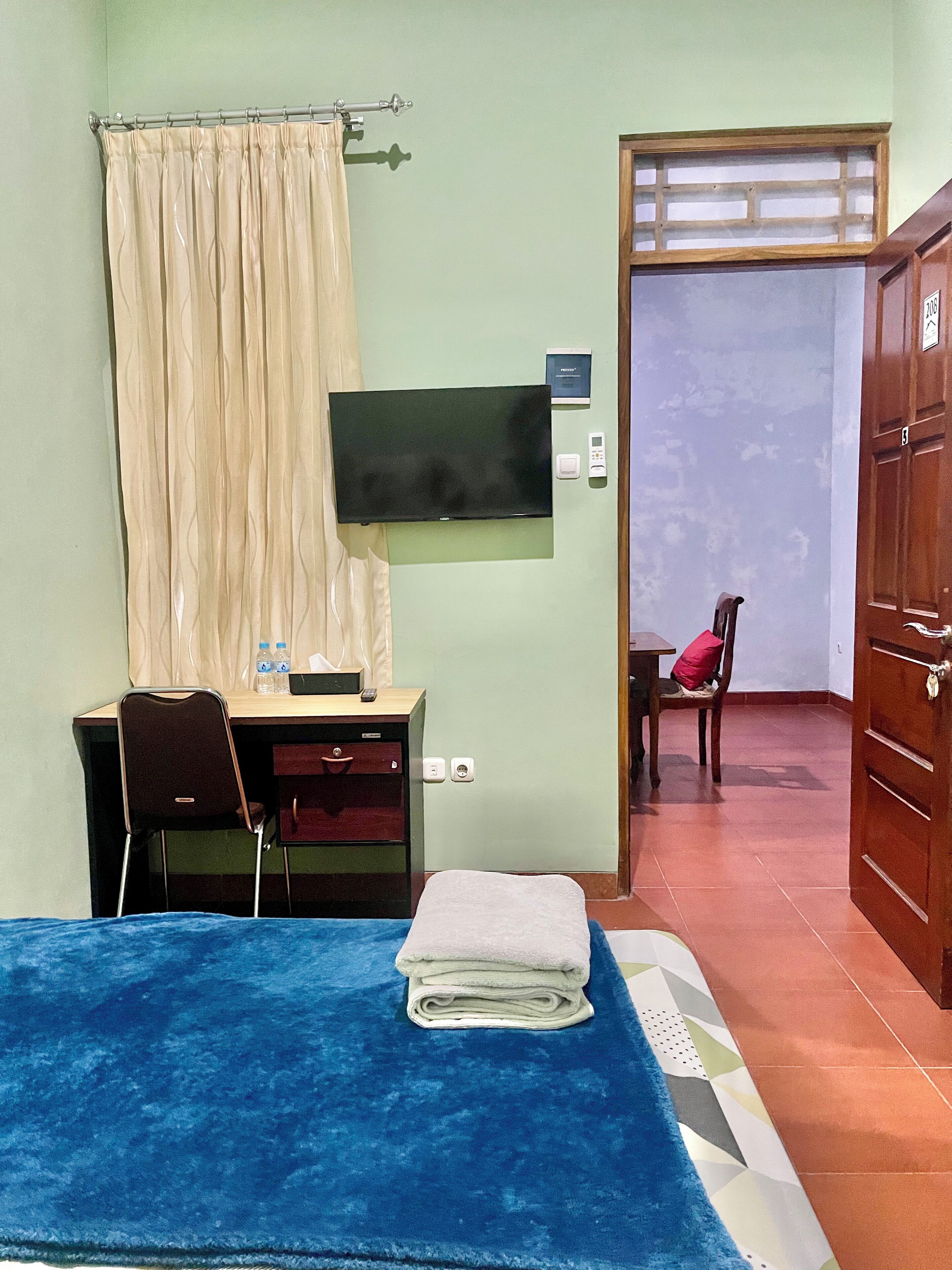 Een kamer met een bed, een bureau met stoel, een televisie en een deur naar een andere kamer.