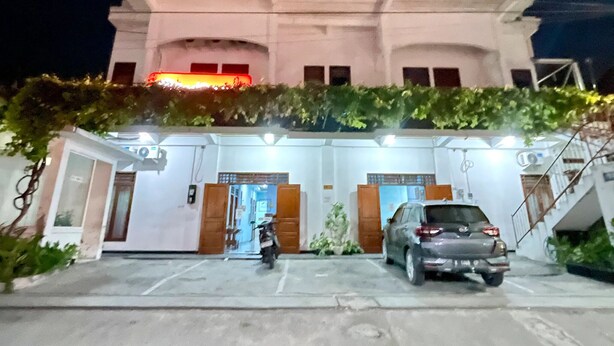 A building with a white facade, a covered entrance, and a parking area with a motorcycle and a car. - Telu Telu Solo (Surakarta)
