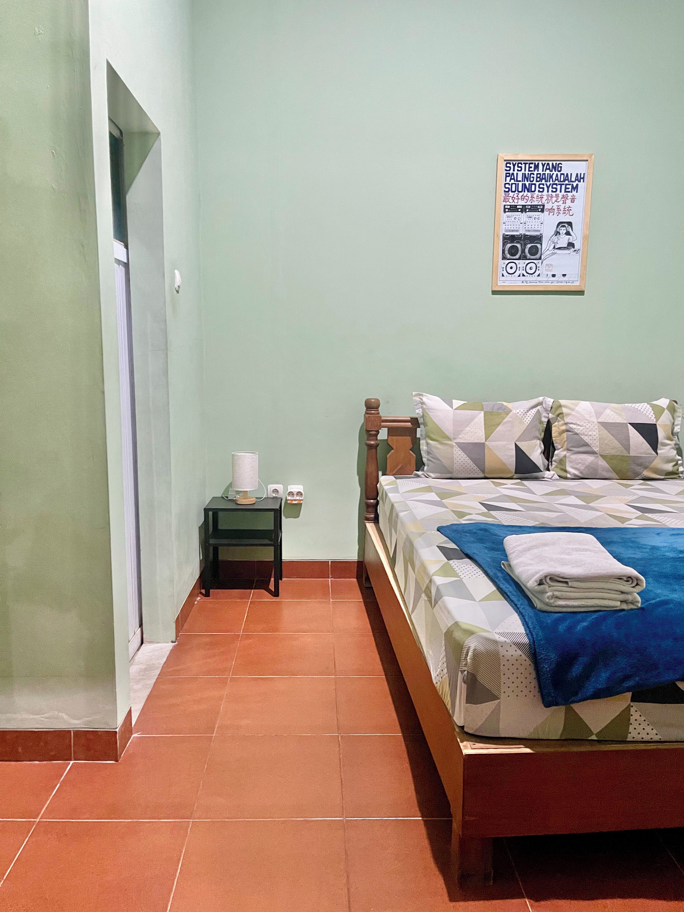 A bedroom with a bed, a nightstand, a poster on the wall, and a door leading to another room.