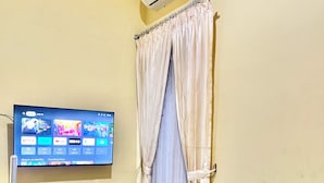 A hotel room with a bed, a TV on a wooden stand, an air conditioner, and a curtain. - Telu Telu Solo (Surakarta)