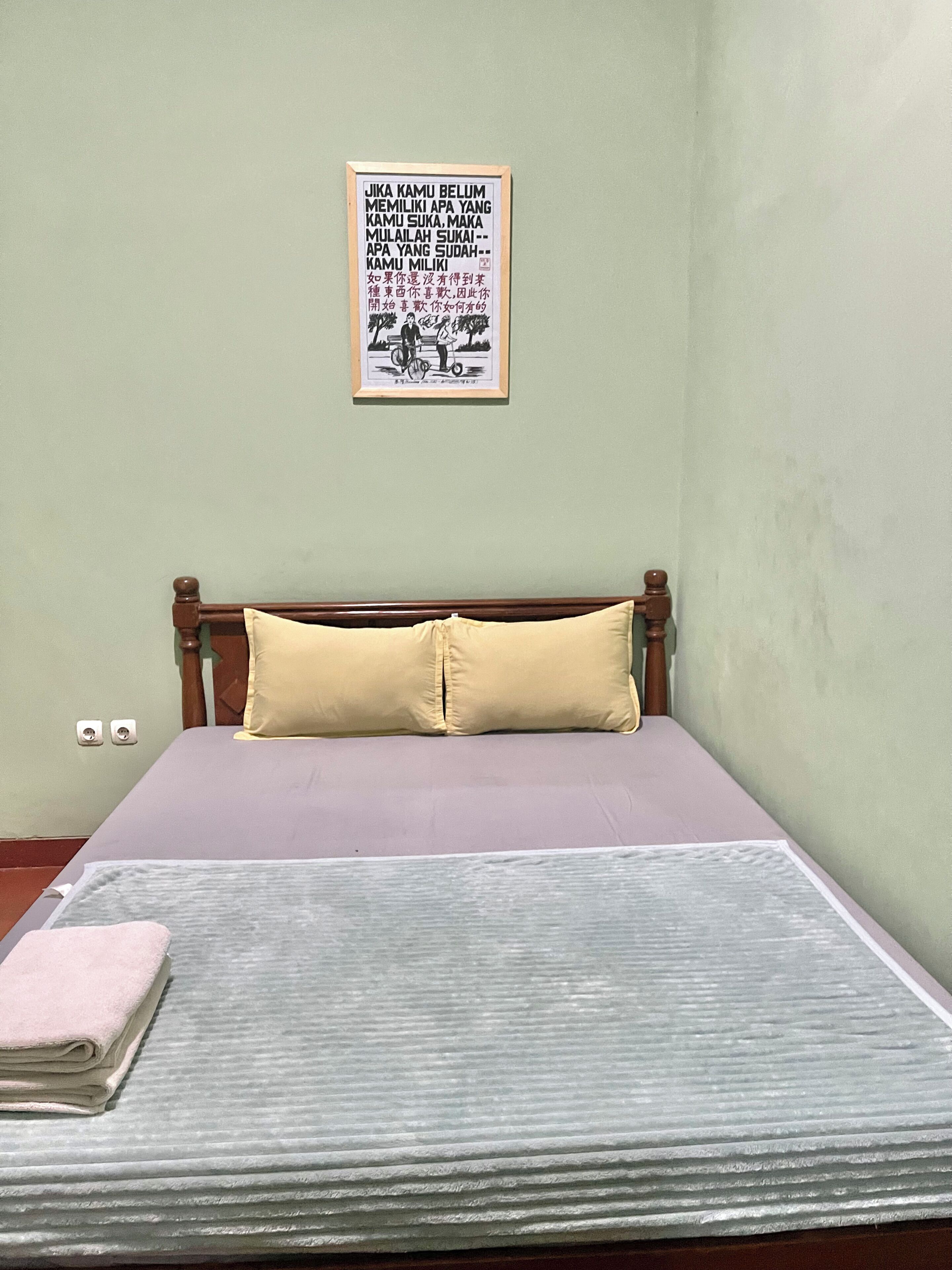 A bed with a wooden headboard, a light-colored mattress, and a single yellow pillow.