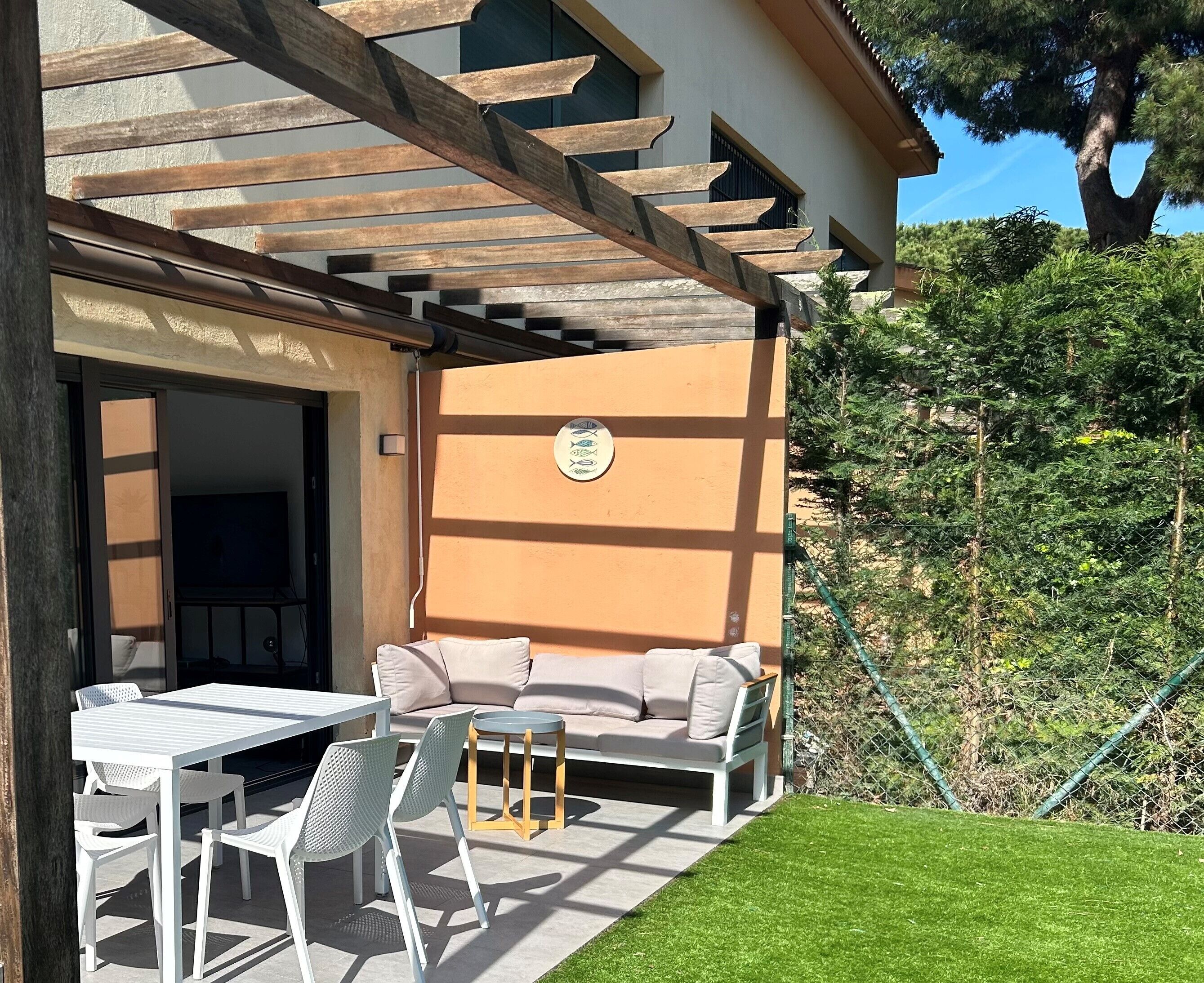 An outdoor patio with a white table and chairs, a beige sofa, and a wooden pergola.