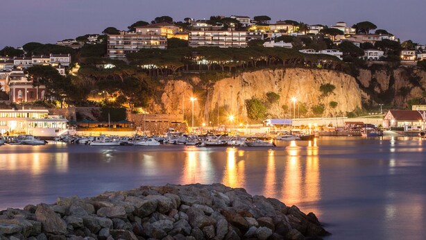 A coastal town at dusk with a marina, rocky shoreline, and buildings with balconies overlooking the water. - Preciosa Casa, con Enorme Piscina en Zona Tranquila y Familiar (Sant Feliu de Guixols)