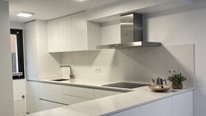 A modern kitchen with white cabinetry, a stainless steel range hood, and a small island with a sink. - Preciosa Casa, con Enorme Piscina en Zona Tranquila y Familiar (Sant Feliu de Guixols)